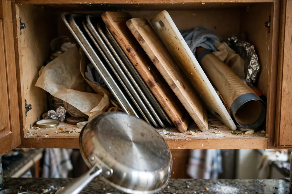 Leaning stack of baking sheets and cutting boards sliding out of a kitchen cabinet