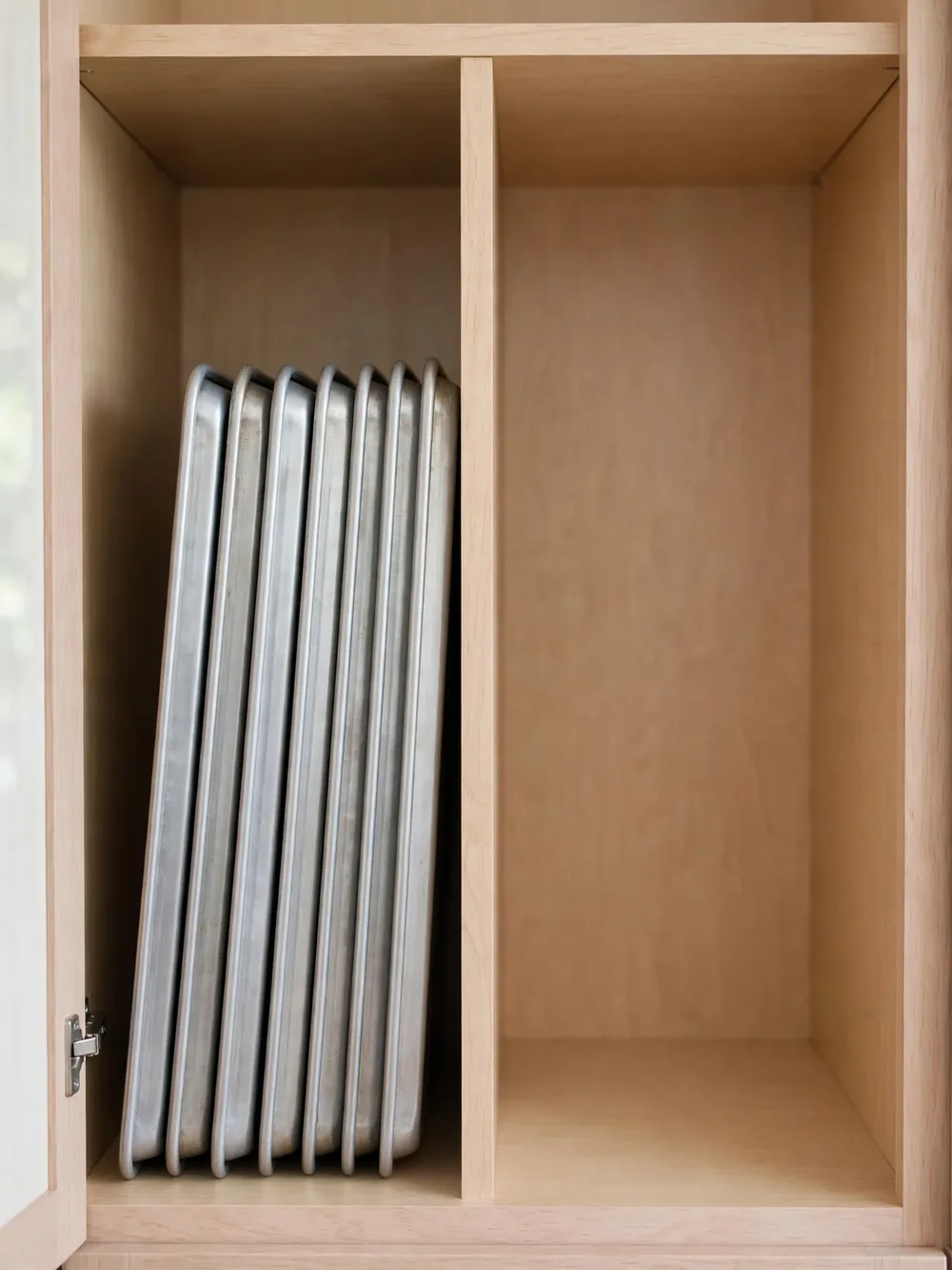 Single vertical divider in an open kitchen cabinet with neatly filed baking sheets