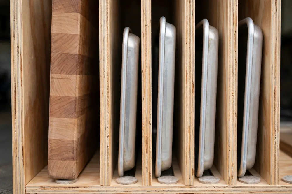 Thick wood cutting board in a wide divider slot beside thin aluminum baking sheets in narrow slots