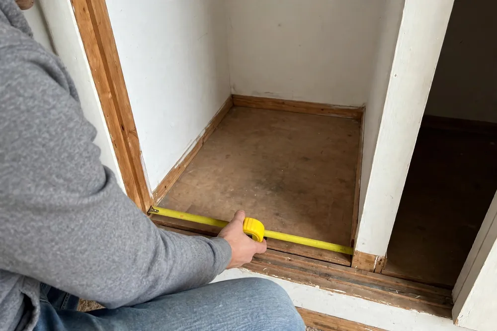 Measuring a small closet floor gap with a tape measure before buying a shoe rack