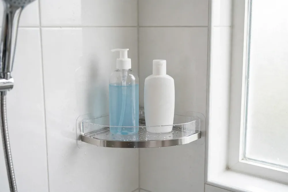 Adhesive corner shower shelf on smooth tile holding body wash and face wash bottles