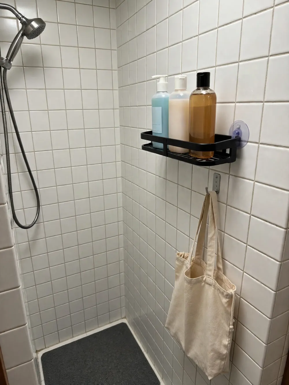 Small dorm shower with one suction shelf holding three bottles and a hanging tote