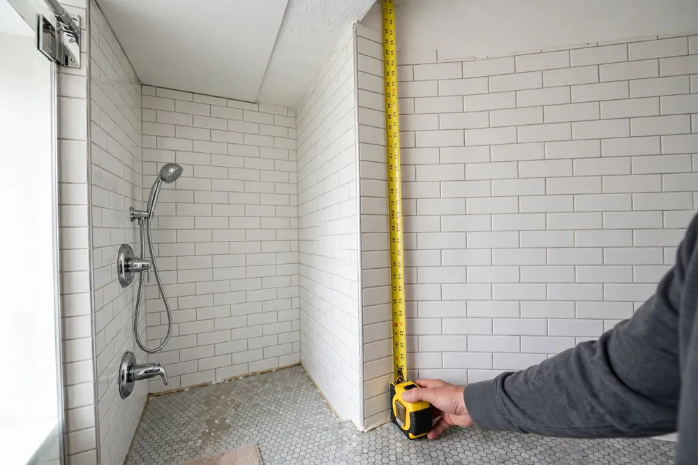 Measuring shower wall height with a tape measure from floor to ceiling in a bathroom corner