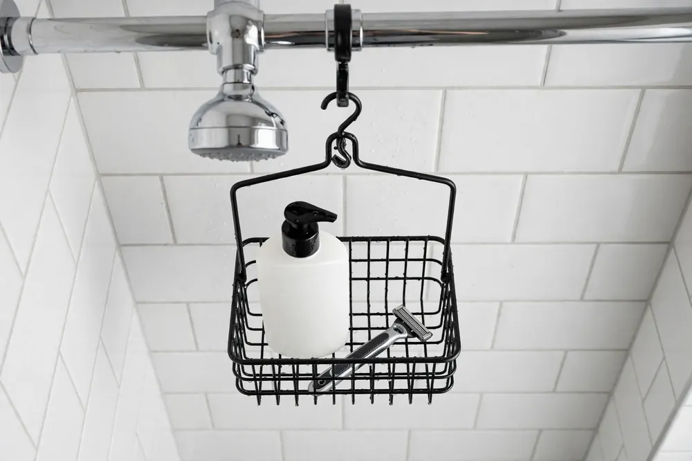 Over the showerhead caddy hanging from a chrome showerhead pipe holding a shampoo bottle and razor