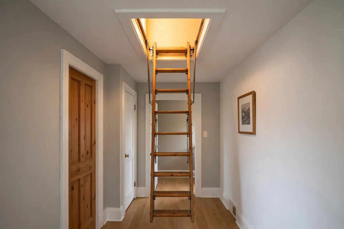 Wooden pull-down attic ladder extended from a ceiling hatch with light from above.