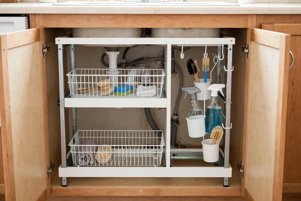 Puricon white two-tier pull-out under sink organizer with hooks and hanging cups in a kitchen cabinet