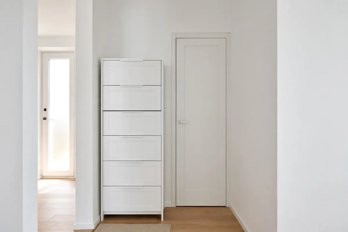Slim white tilt-out shoe cabinet in a narrow hallway next to a small closet