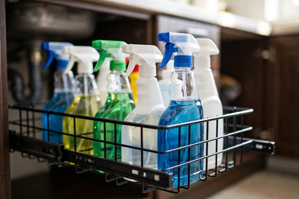 Black metal pull-out under sink rack with wire baskets of cleaning spray bottles