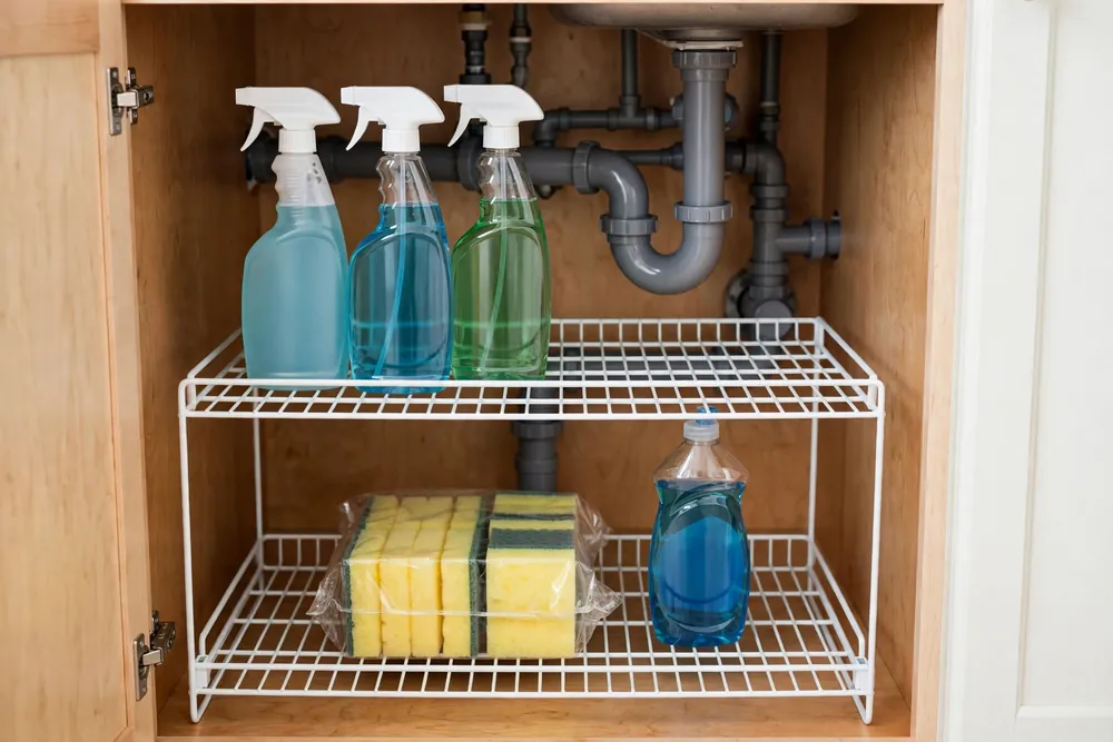 Two-level shelf riser under a kitchen sink doubling storage space for short bottles