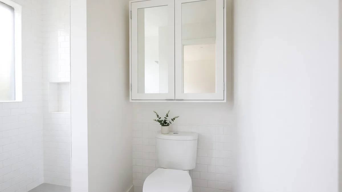 White wall-mounted bathroom cabinet with mirrored doors above a toilet